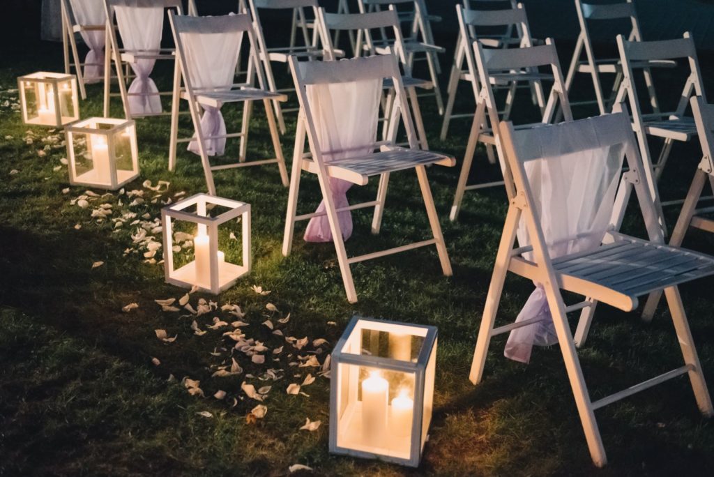 Candle lanterns next to white chairs at a DIY wedding.